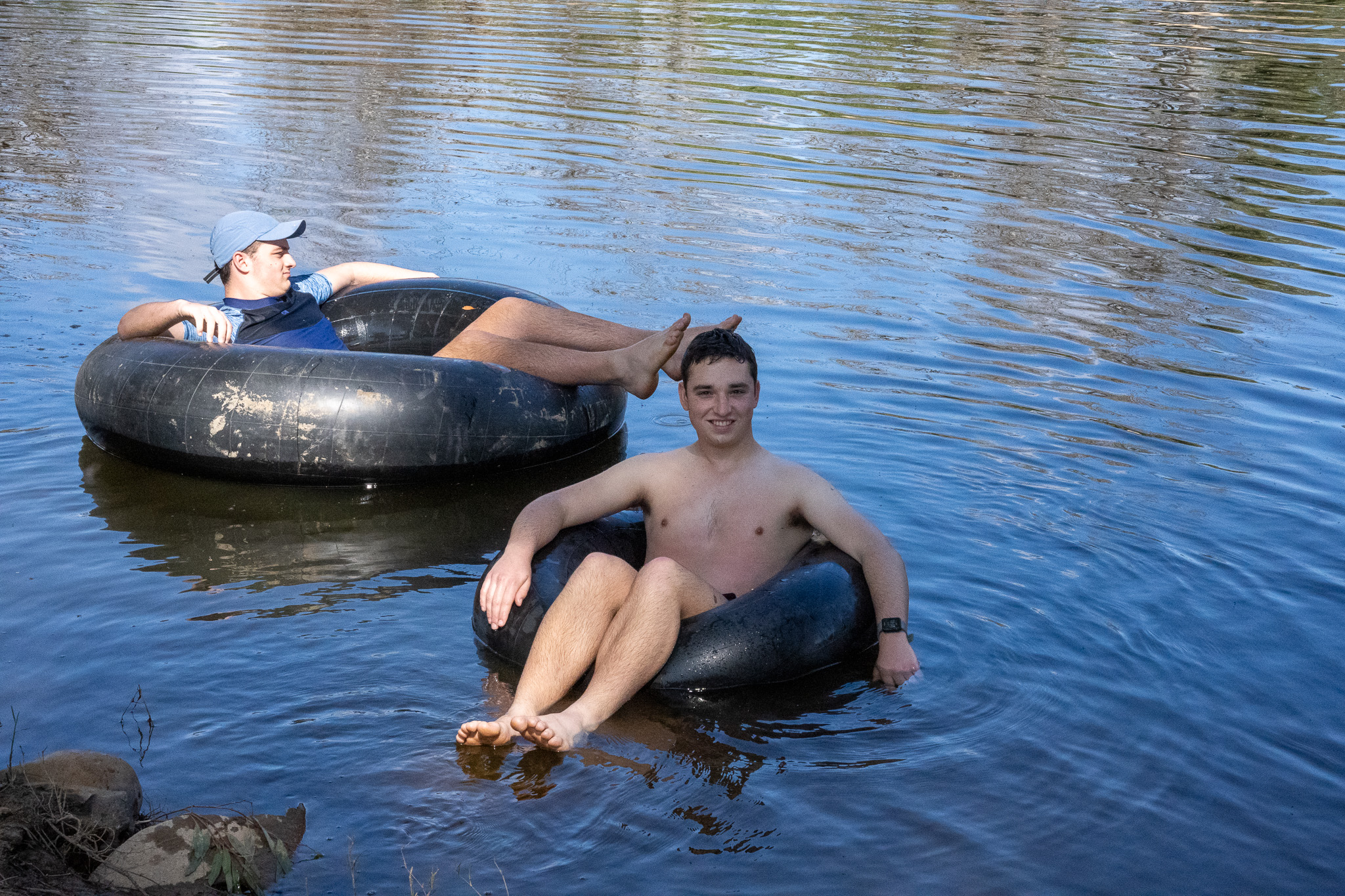 River Tubing Relaxation Two young men relaxing in inner tubes on a calm river, enjoying a warm day.