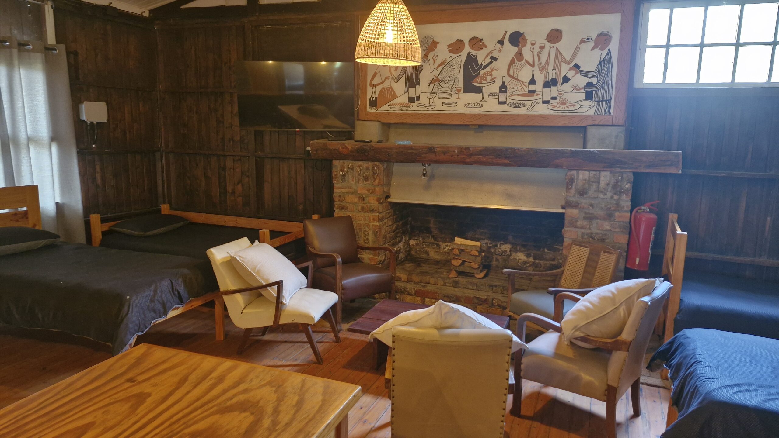 Group of people playing volleyball on a grassy area with a wooden bench labeled "DIE HOUTHUIS" in the foreground and dogs resting nearby.