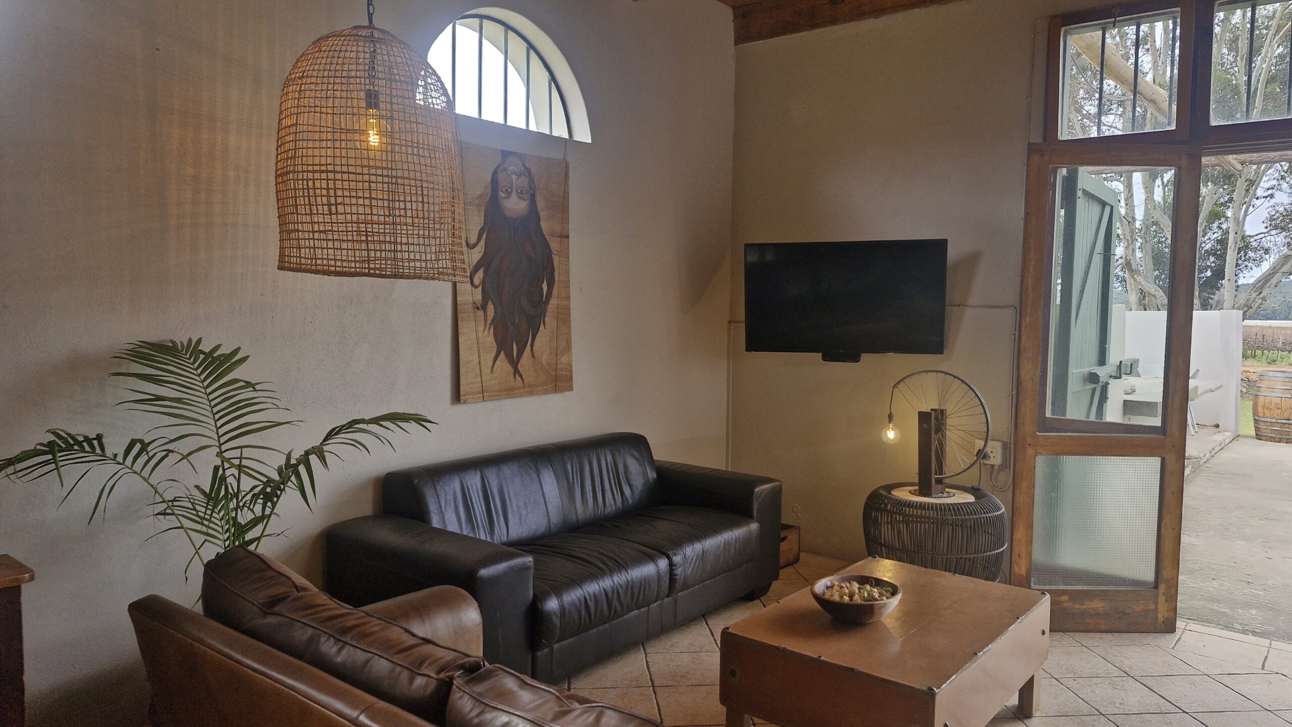Cozy indoor lounge area with leather sofas, wall art, hanging woven light fixture, and a TV on the wall.
